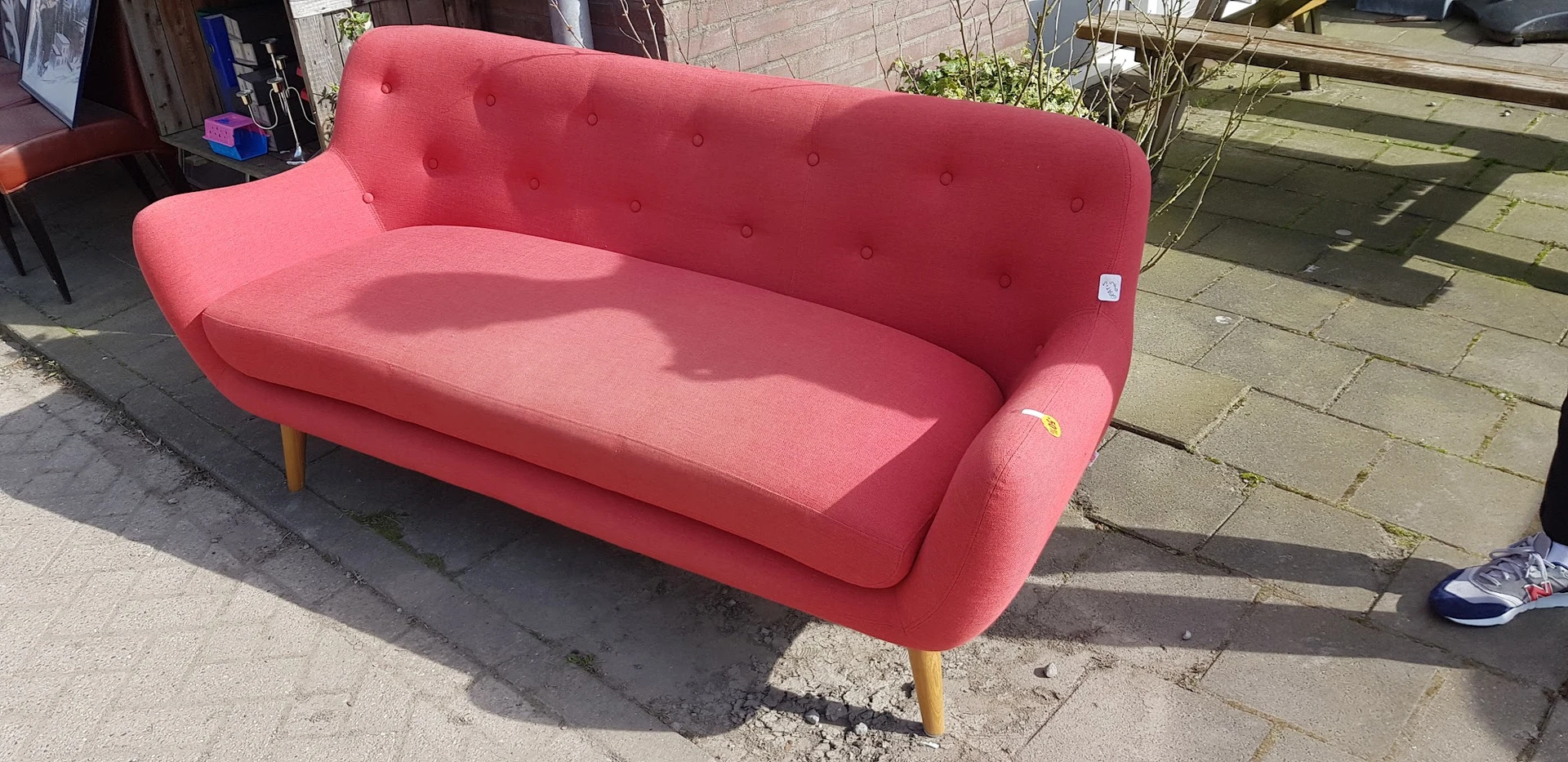 Roze/rood fauteuil met knopen en houten poten op een terras
