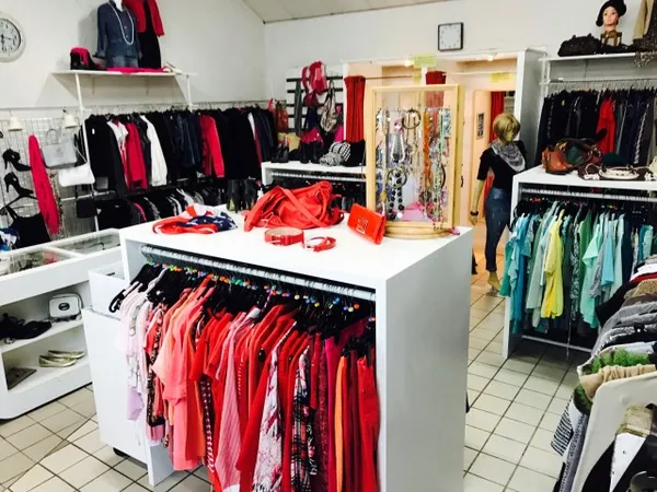 Overzicht van kringloopwinkel met kledingrekken, stellingen en uitgestalde spullen in verschillende kleuren