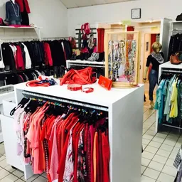 Overzicht van kringloopwinkel met kledingrekken, stellingen en uitgestalde spullen in verschillende kleuren