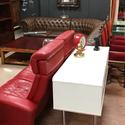 Zithoek met bruine chesterfield bank, rode leren stoelen en witte salontafel met rode klok