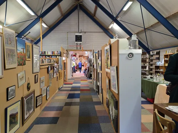 Lange gang in kringloopwinkel met kunstwerken aan de muren, boekenkasten en stellingen met spullen aan beide zijden