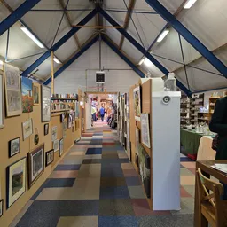 Lange gang in kringloopwinkel met kunstwerken aan de muren, boekenkasten en stellingen met spullen aan beide zijden