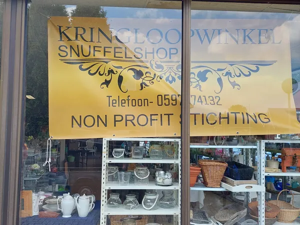 Winkelruit met gele en witte borden met winkelnaam, telefoonnummer en 'non profit stichting' opschrift. Achter het glas zijn 