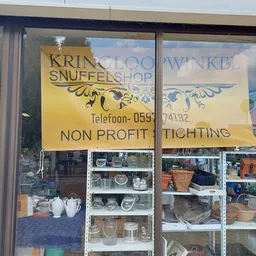 Winkelruit met gele en witte borden met winkelnaam, telefoonnummer en 'non profit stichting' opschrift. Achter het glas zijn 