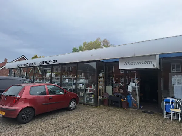 Voorgevel van kringloopwinkel met winkelpui, etalage en rode auto op parkeerplaats