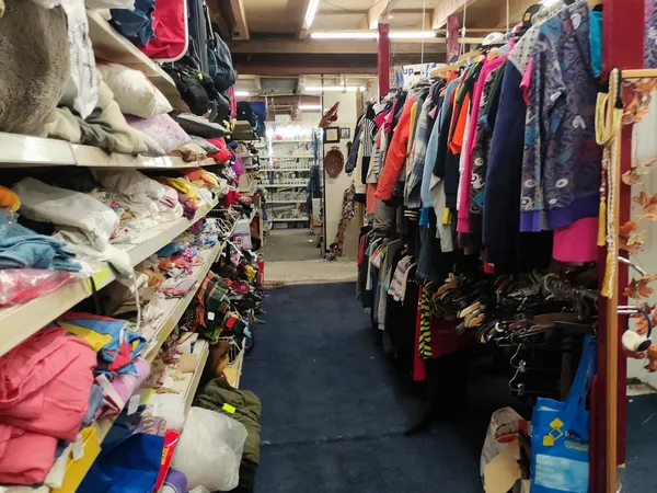 Winkelinterieur met kledingrekken en stapels textiel aan beide zijden van een gangpad