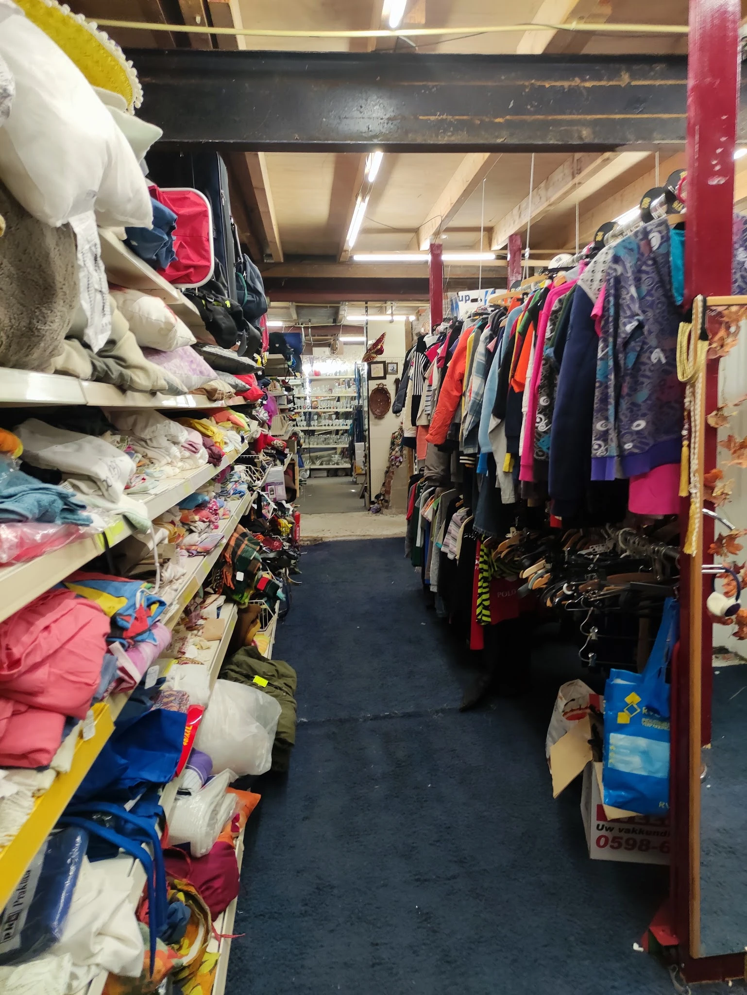 Winkelinterieur met kledingrekken en stapels textiel aan beide zijden van een gangpad