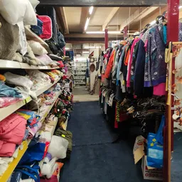 Winkelinterieur met kledingrekken en stapels textiel aan beide zijden van een gangpad