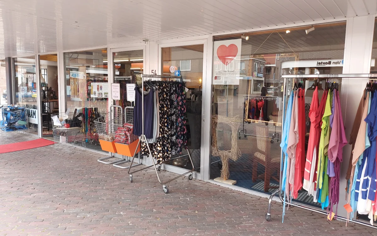 Winkelgevel met etalages vol kleding en accessoires, rode deurmat zichtbaar