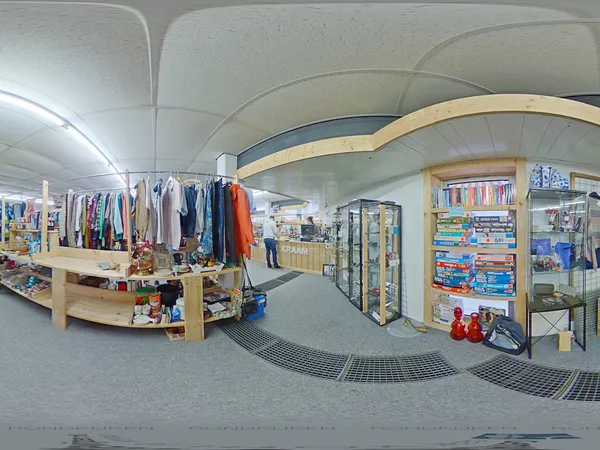 Overzicht van kringloopwinkel met kledingrekken, boekenkasten en diverse spullen uitgestald op de vloer
