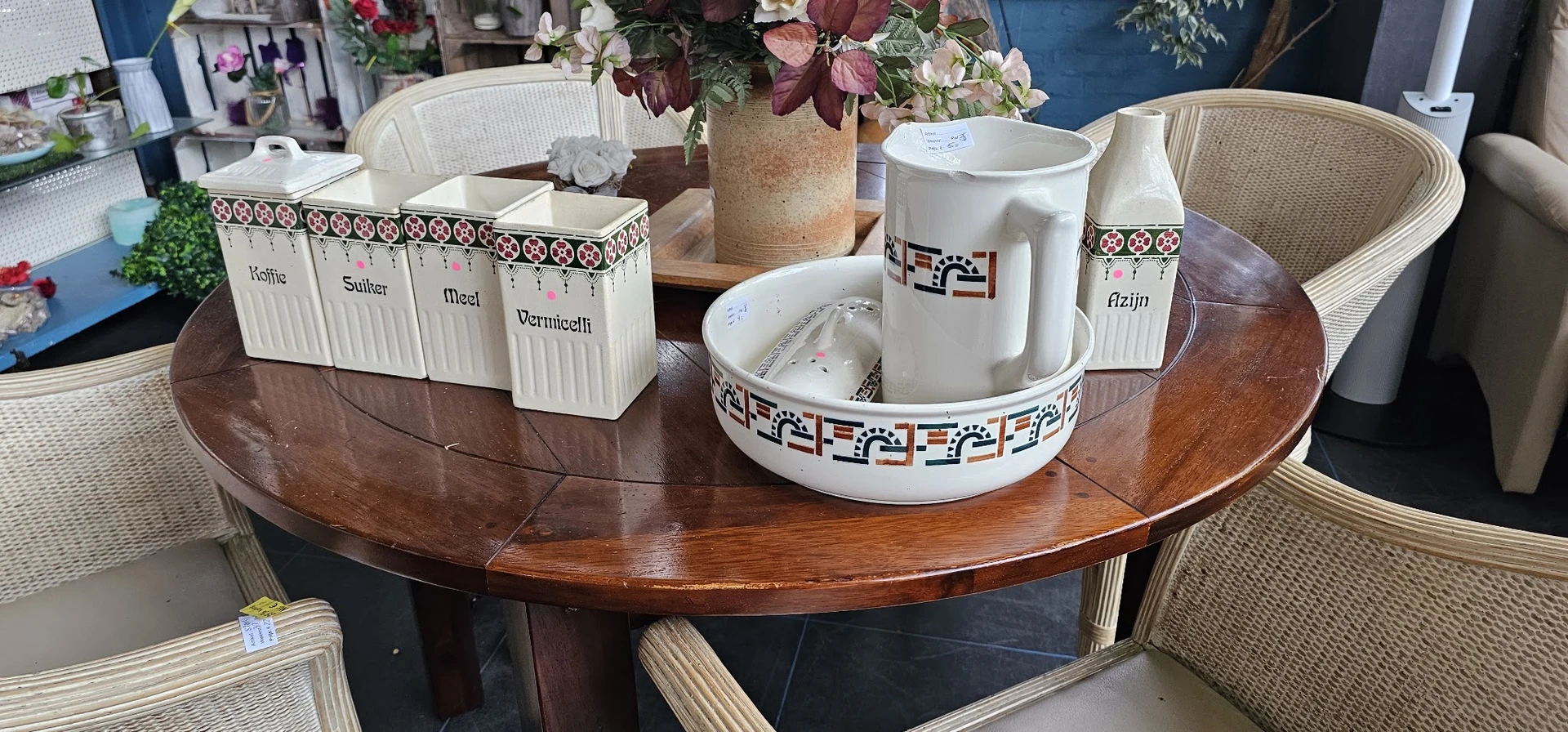 Ronde houten tafel met wit servies, bloemen in vaas en witte potten met etiketten