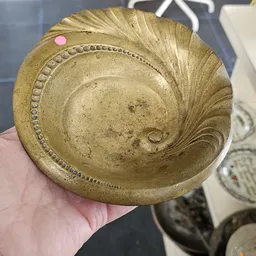 Goudkleurige decoratieve schaal met spiraal- en sierornamenten, in hand gehouden