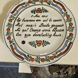 Decoratief aardewerk bord met Nederlands gedicht uit 1945 en siermotieven met oranje bloemen
