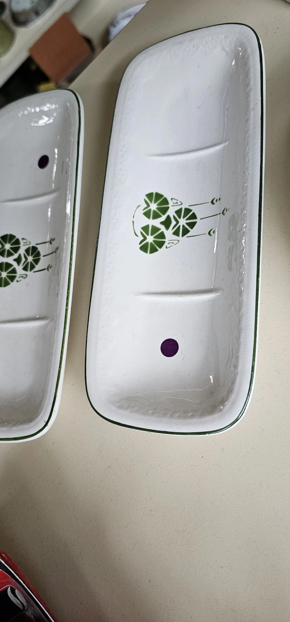 Twee witte serviesschalen met groen blad-patroon en een donkerpaarse stip
