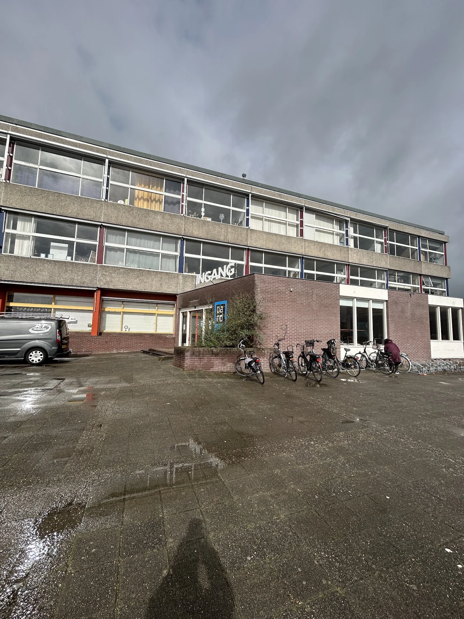 Voorkant van kringloopwinkel met ingang, grote ramen, bakstenen gevel en fietsen geparkeerd ervoor