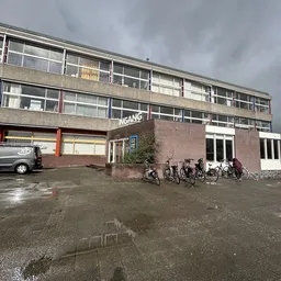 Voorkant van kringloopwinkel met ingang, grote ramen, bakstenen gevel en fietsen geparkeerd ervoor
