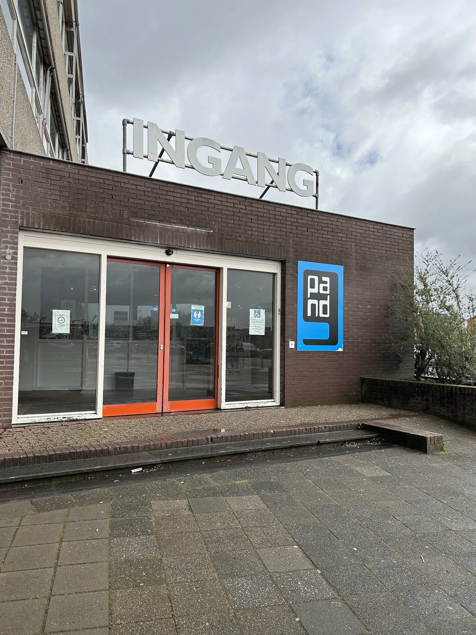 Bakstenen gevel van kringloopwinkel met glazen deuren met oranje kozijn en blauwe Dano-logo