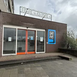 Bakstenen gevel van kringloopwinkel met glazen deuren met oranje kozijn en blauwe Dano-logo