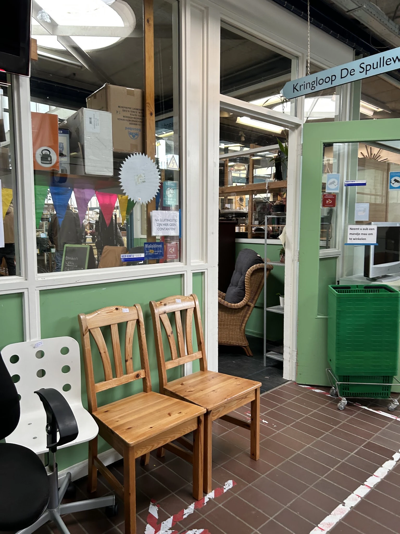 Winkelvoorgevel met groene frame, houten stoelen buiten, en binnenkant zichtbaar door glasruit