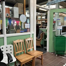 Winkelvoorgevel met groene frame, houten stoelen buiten, en binnenkant zichtbaar door glasruit