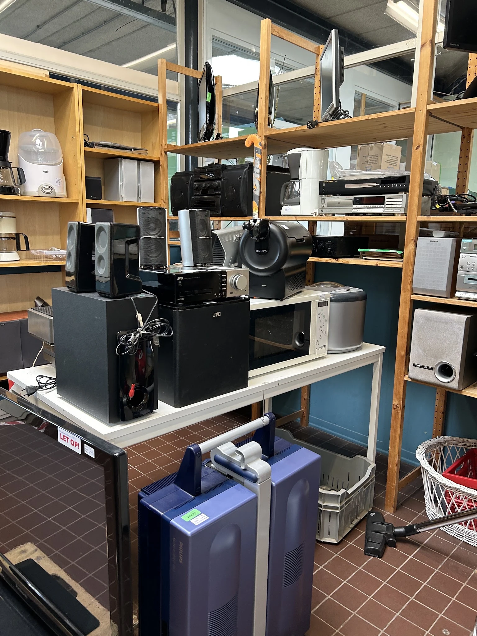 Tafel met verschillende elektronische apparaten zoals speakers, versterkers en audiokasten in een kringloopwinkel