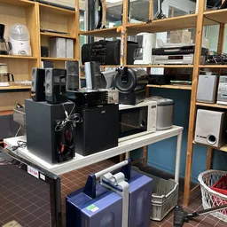 Tafel met verschillende elektronische apparaten zoals speakers, versterkers en audiokasten in een kringloopwinkel