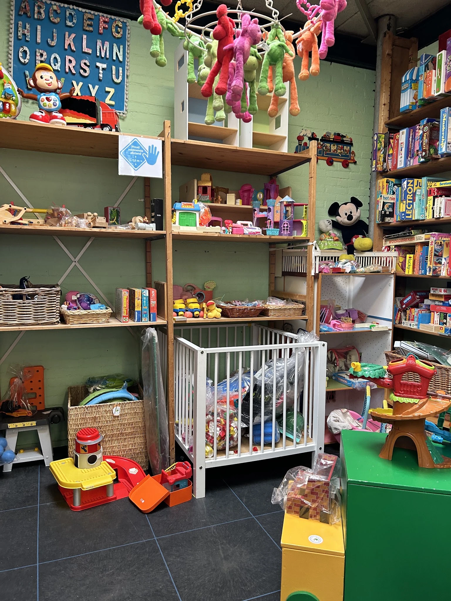 Kinderspeelgoedafdeling met open kasten, speelgoed, boeken, een babybox en een grote pluchen Mickey Mouse knuffel