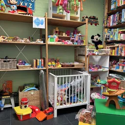 Kinderspeelgoedafdeling met open kasten, speelgoed, boeken, een babybox en een grote pluchen Mickey Mouse knuffel