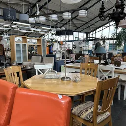 Winkelvloer met houten eettafel, stoelen en huisraad in een grote hal met industrieel plafond