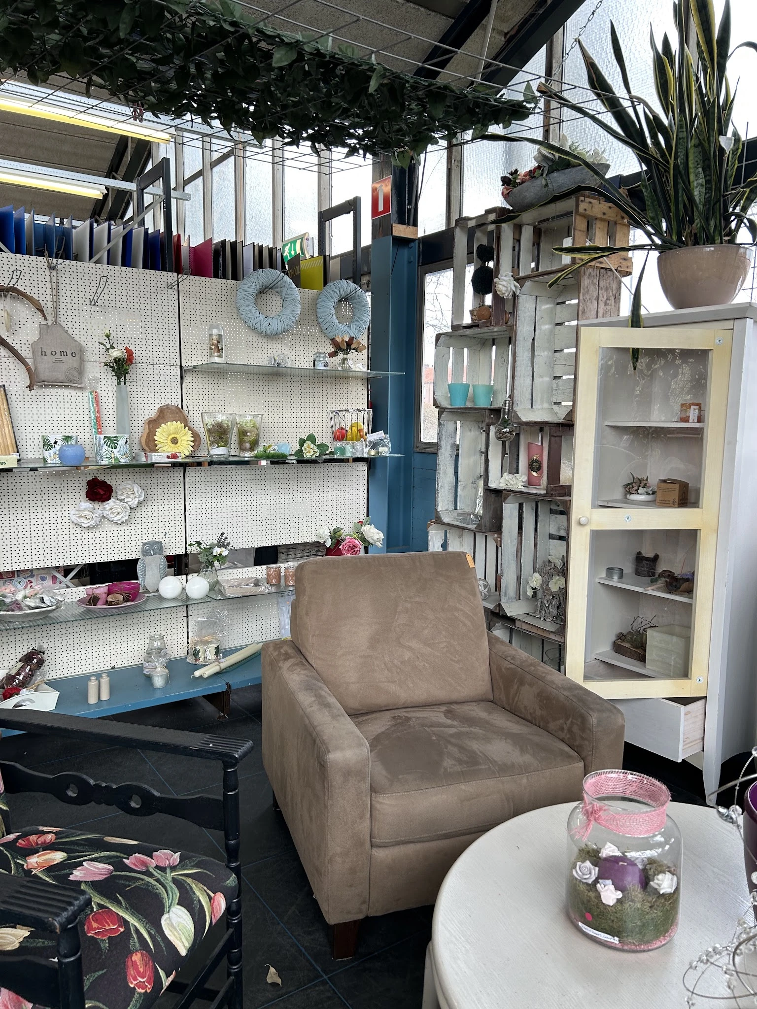 Binnenkant van kringloopwinkel met grijze fauteuil, witte stellingen met decoratie-items, kasten en hangend huisraad