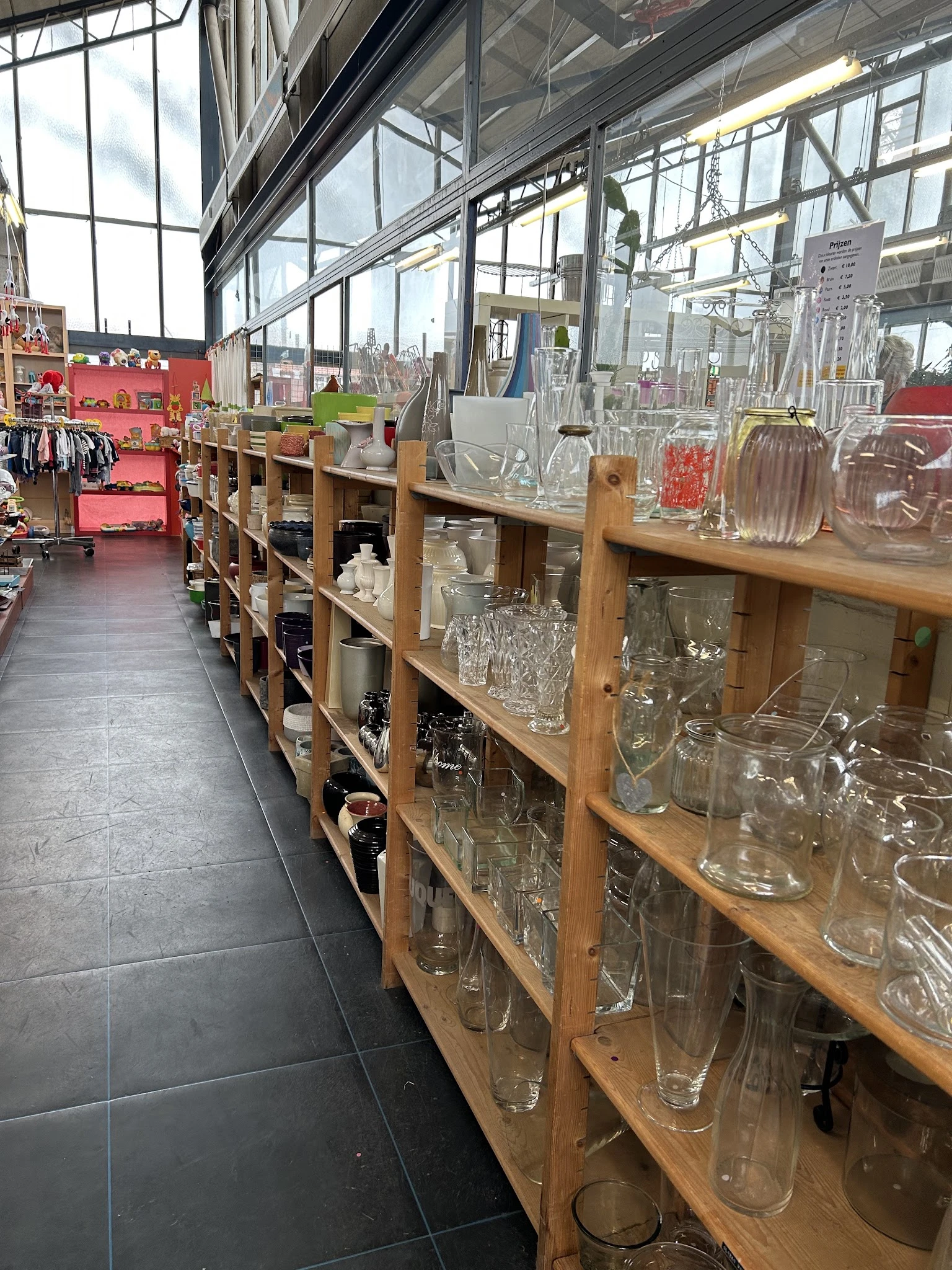 Houten stellingen met diverse glazen artikelen en huishoudelijke spullen in een kringloopwinkel