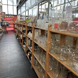Houten stellingen met diverse glazen artikelen en huishoudelijke spullen in een kringloopwinkel