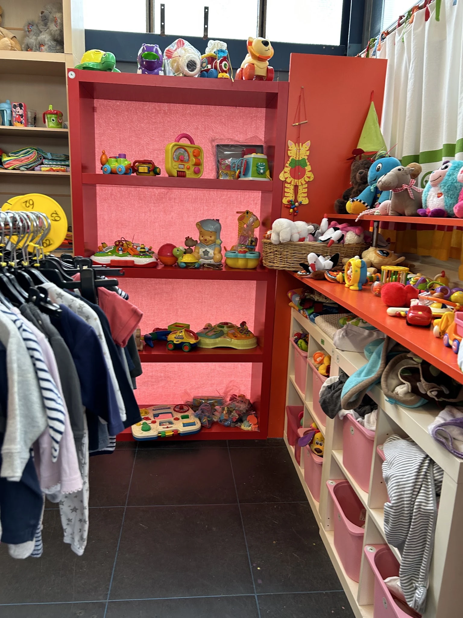 Rode stellingen met speelgoed, knuffels en huishoudartikelen, links daarnaast kleding aan hangers