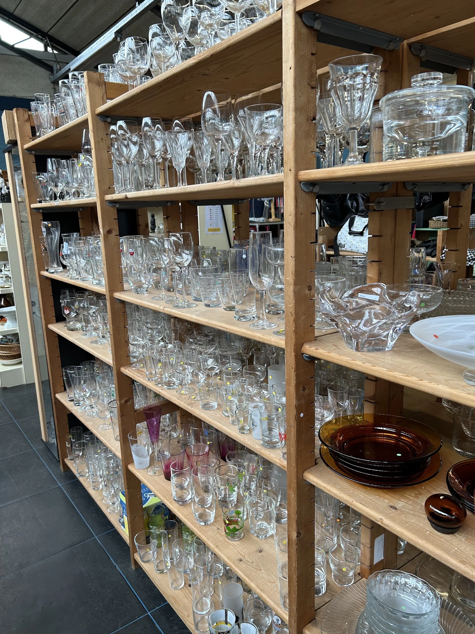 Houten stellingen vol met glazenwerk en serviesgoed in de kringloopwinkel