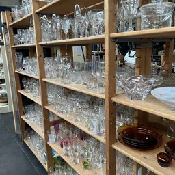 Houten stellingen vol met glazenwerk en serviesgoed in de kringloopwinkel