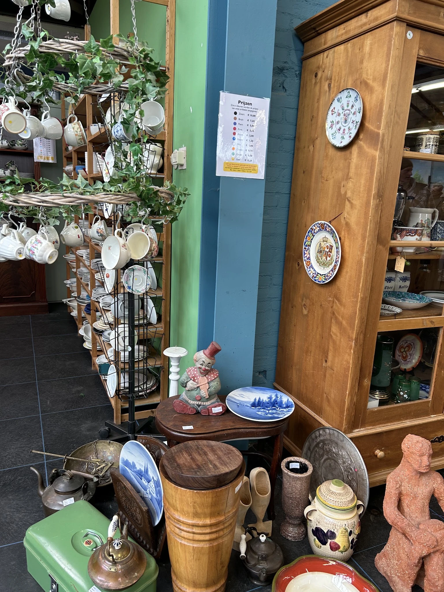 Uitgestalde serviesgoed en decoratieve borden in de kringloopwinkel, met stellingen vol kopjes en schotels