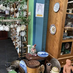 Uitgestalde serviesgoed en decoratieve borden in de kringloopwinkel, met stellingen vol kopjes en schotels