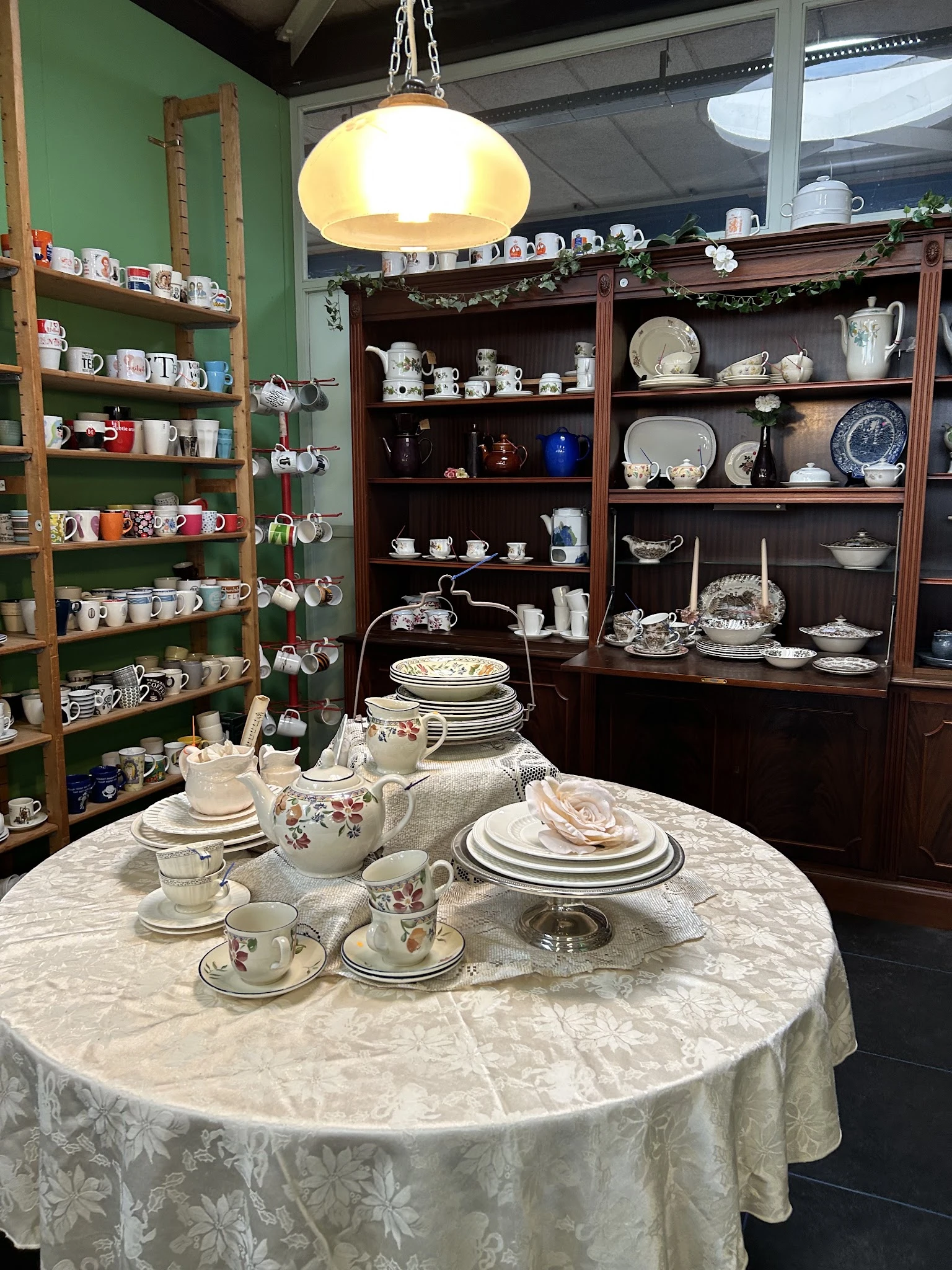 Uitgestalde serviesgoed en tafelgerei in een kringloopwinkel, met op de voorgrond een gedekte tafel met porselein en op de ac