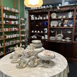 Uitgestalde serviesgoed en tafelgerei in een kringloopwinkel, met op de voorgrond een gedekte tafel met porselein en op de ac
