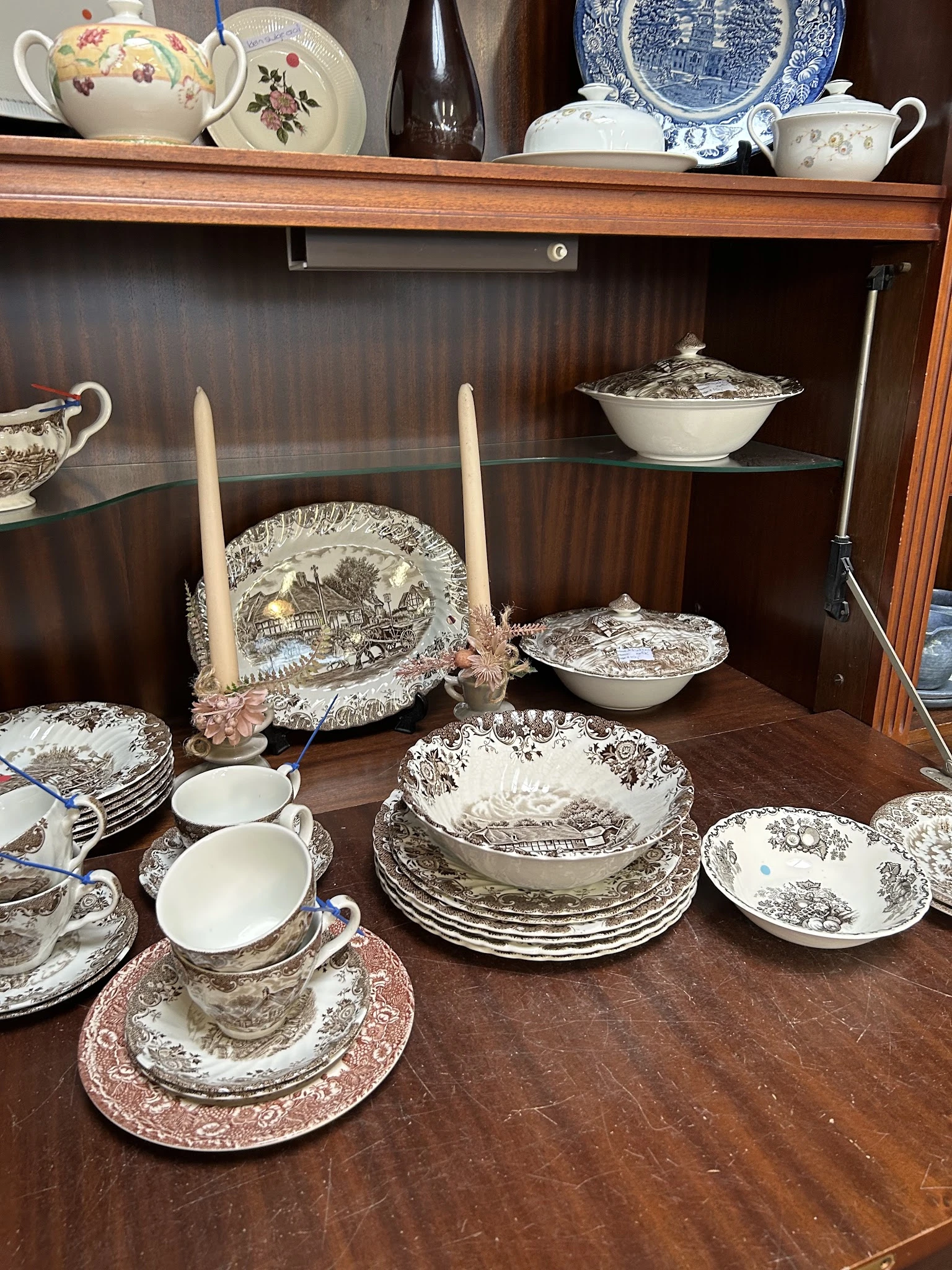 Vitrinekast met antiek servies: potten, borden, kandelaars en decoratieve stukken met klassieke print