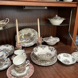 Vitrinekast met antiek servies: potten, borden, kandelaars en decoratieve stukken met klassieke print