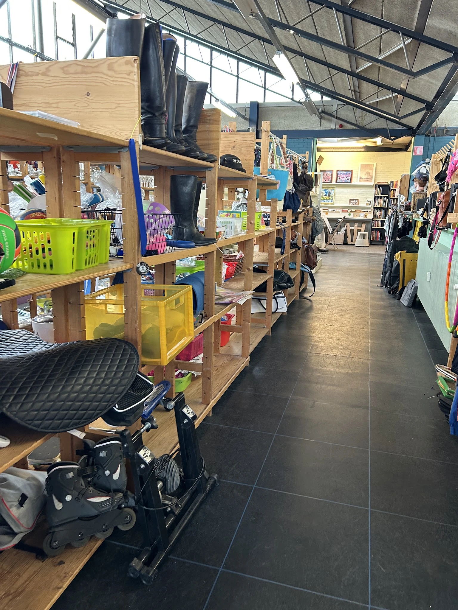 Winkelvloer met houten stellingen, gele en groene opbergkratten, fietsen en diverse spullen in een kringloopwinkel