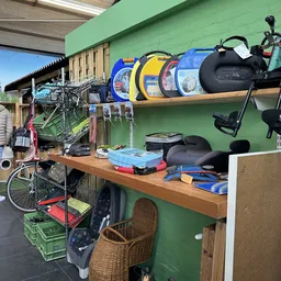 Werkbank met uitgestalde spullen: fiets, sportrugtassen, fietszadels, toolboxen en ander tweedehandsaanbod