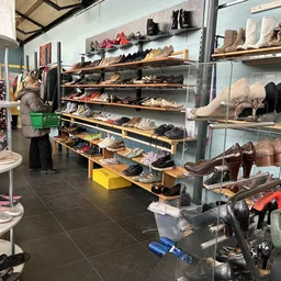 Uitgestalde schoenen op houten stellingen en in vitrinekastjes in een kringloopwinkel