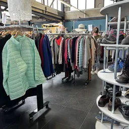 Rekken met tweedehands kleding, waaronder jassen, truien en andere kledingstukken in verschillende kleuren
