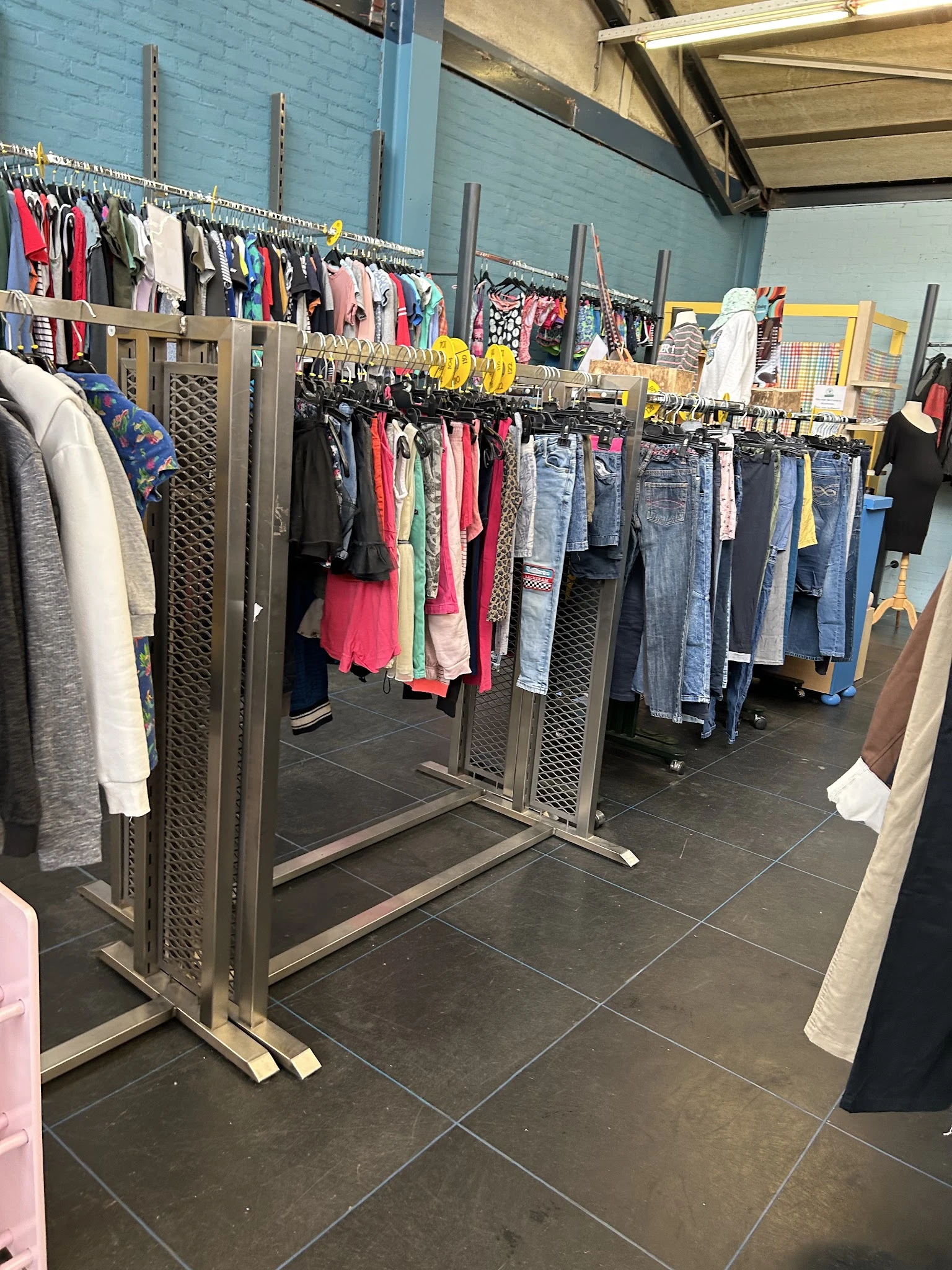 Rekken met tweedehands kleding: jassen, truien, jurken en broeken in verschillende kleuren