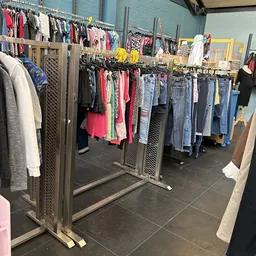 Rekken met tweedehands kleding: jassen, truien, jurken en broeken in verschillende kleuren