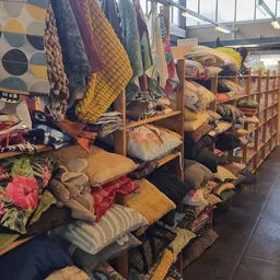 Uitgestalde kussens, plaids en textielwaren op houten stellingen in de winkel