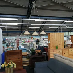 Winkelvloer met houten meubels, lampen, servies en huisraad uitgestald; stellingen en werkplaats op achtergrond