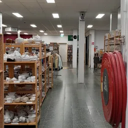 Winkelinterieur met houten stellingen vol servies, kleding aan rekken, boekenkasten en een rode brand-slang aan de rechterkan